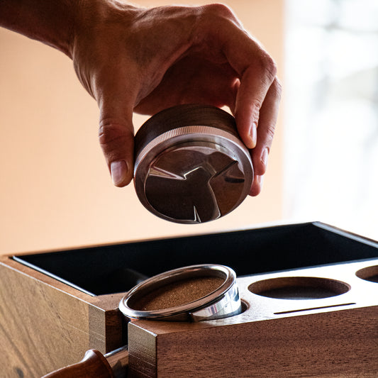 Hand holding a wooden coffee distributor near tamping station and portafilter