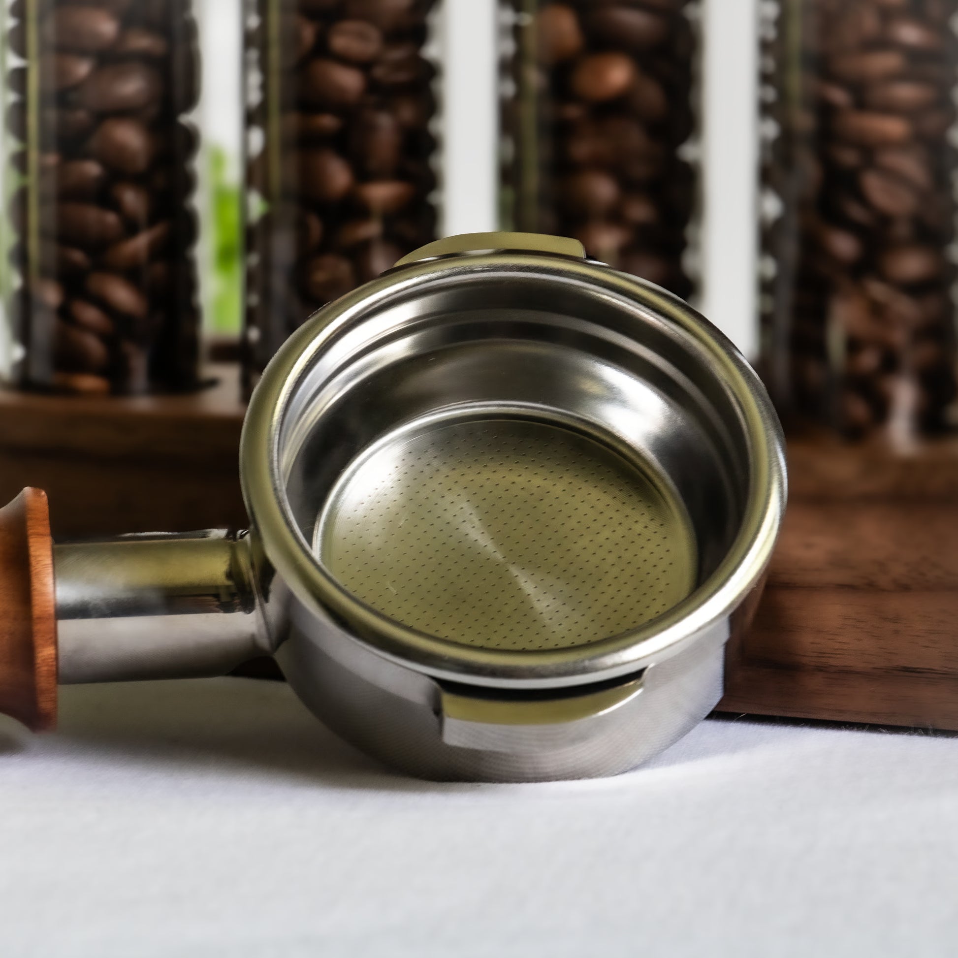 Metal double espresso cup with wooden handle on a white surface, coffee beans in the background