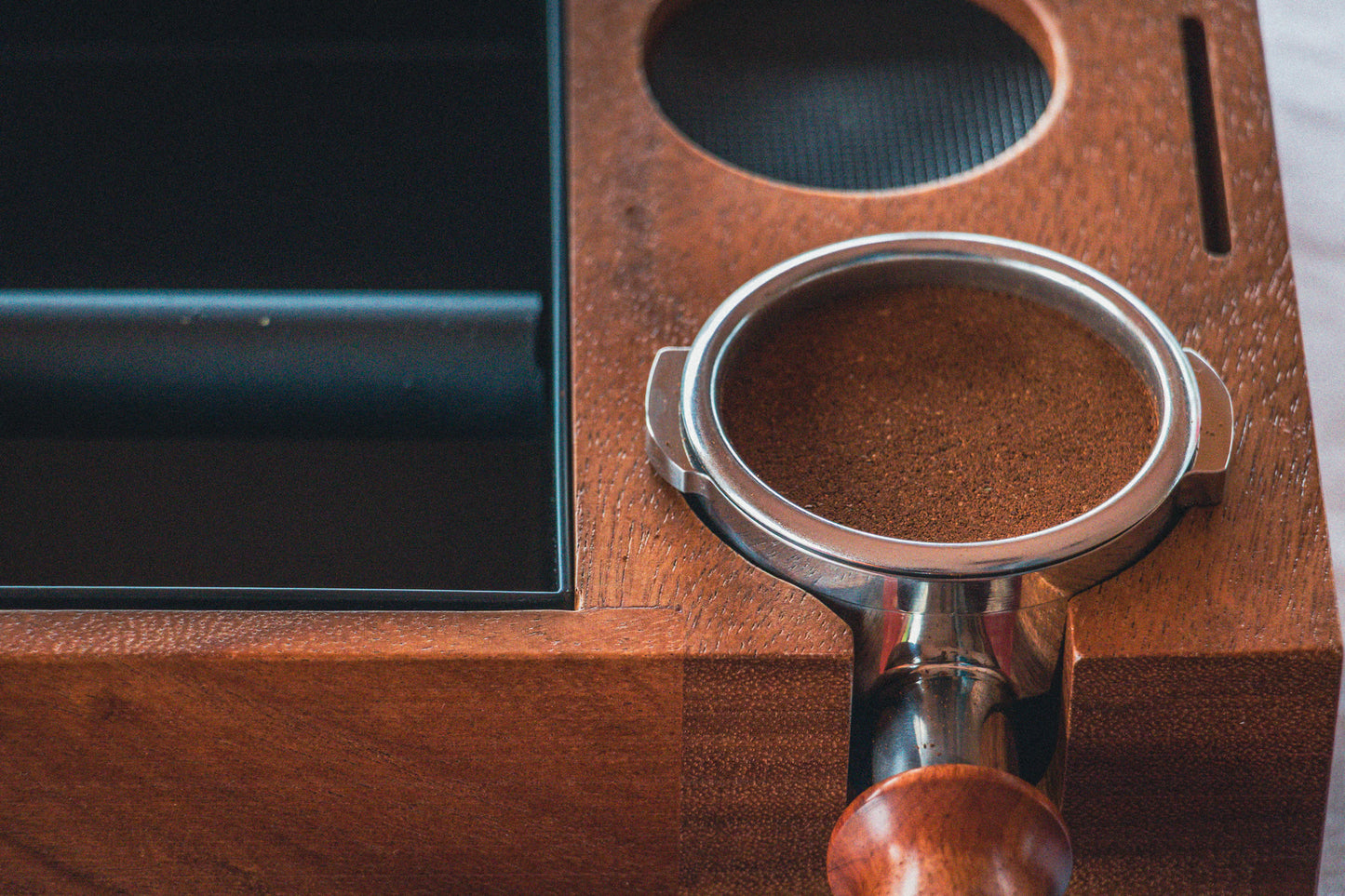 Close up of distributed coffee in portafilter placed on wooden tamping station