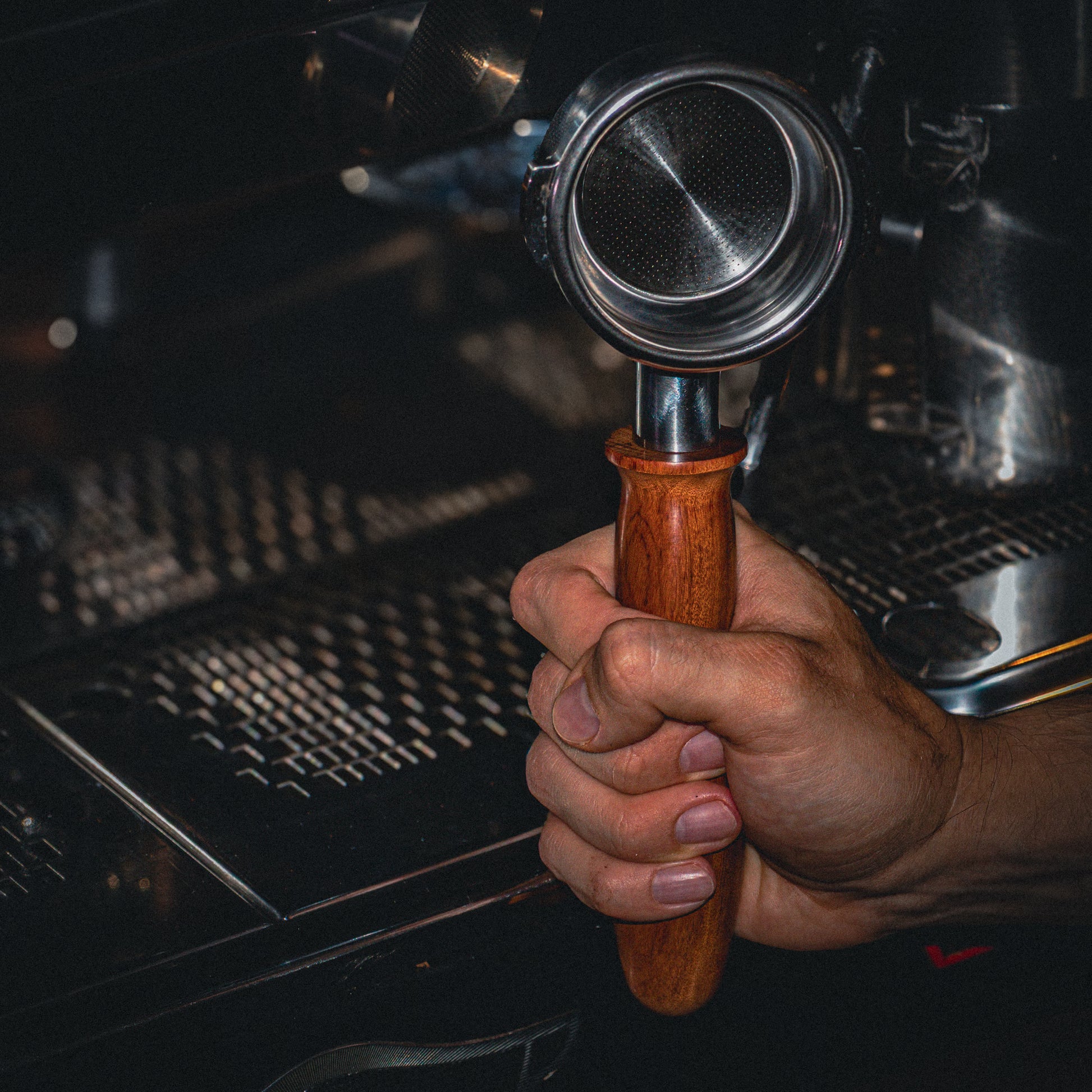 Hand holding a wooden-handled portafilter against a espresso machine background
