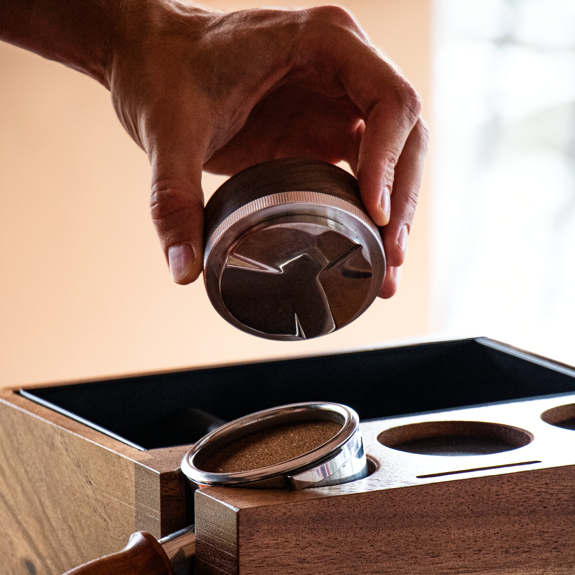 Hand holding a wooden coffee distributor  near tamping station and portafilter