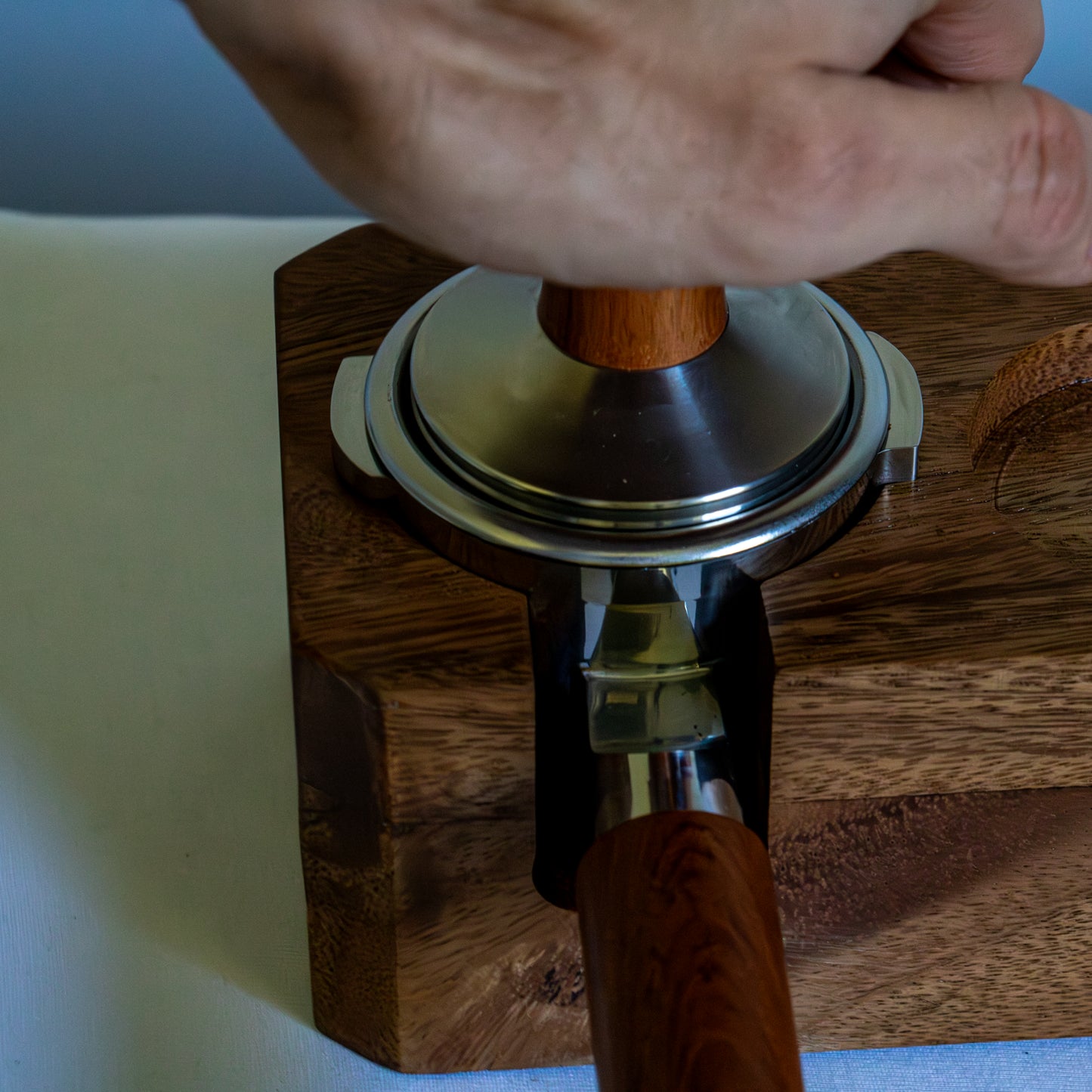 Hand using a wooden coffee tamper on a wooden surface