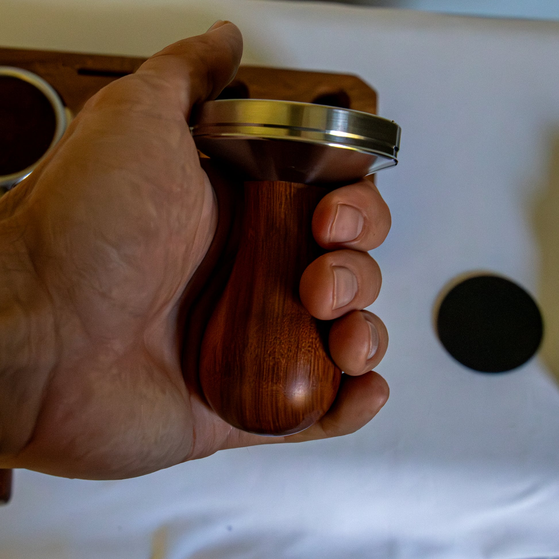 Hand holding a wooden coffee tamp with a blurred background