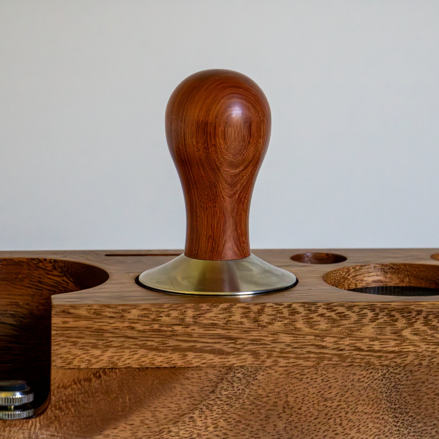Wooden coffee tamp with a metal base on a wooden stand.