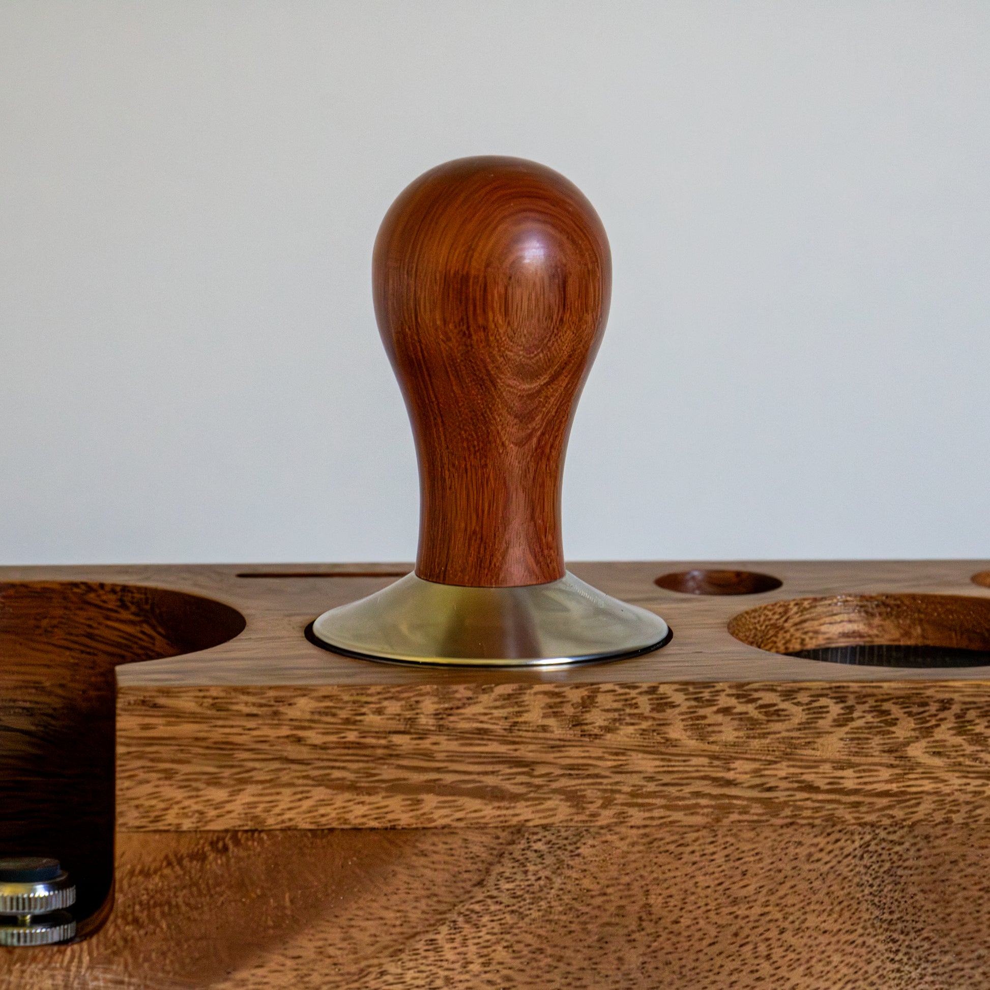 Wooden coffee tamp with a metal base on a wooden stand.
