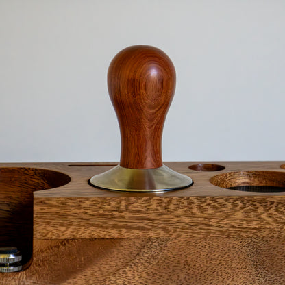 Wooden coffee tamp with a metal base on a wooden stand.